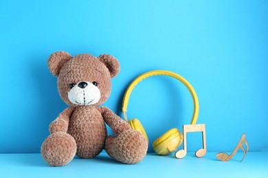 Baby songs. Toy bear, yellow headphones and wooden notes on light blue background