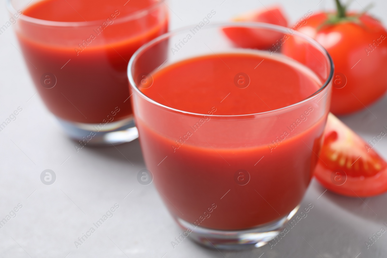 Photo of Delicious fresh tomato juice on light grey table, closeup