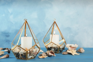 Burning candles in beautiful glass holders with seashells and pebbles on blue wooden table, space for text