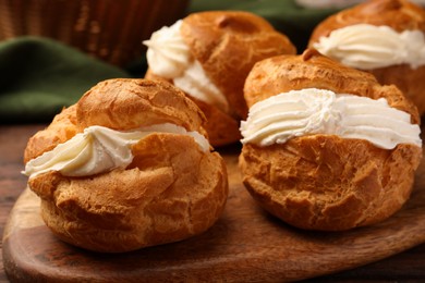 Photo of Delicious profiteroles with cream filling on wooden table, closeup