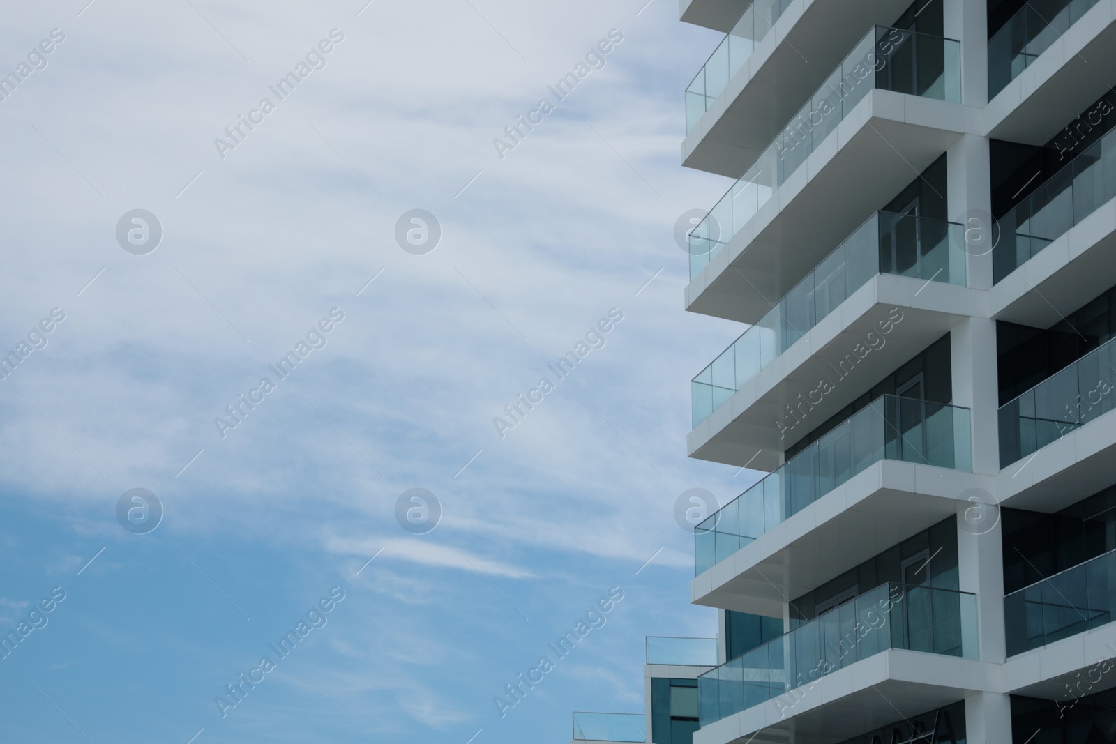 Photo of Exterior of residential building with balconies against blue sky, low angle view. Space for text