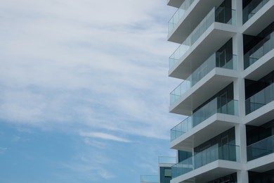 Exterior of residential building with balconies against blue sky, low angle view. Space for text