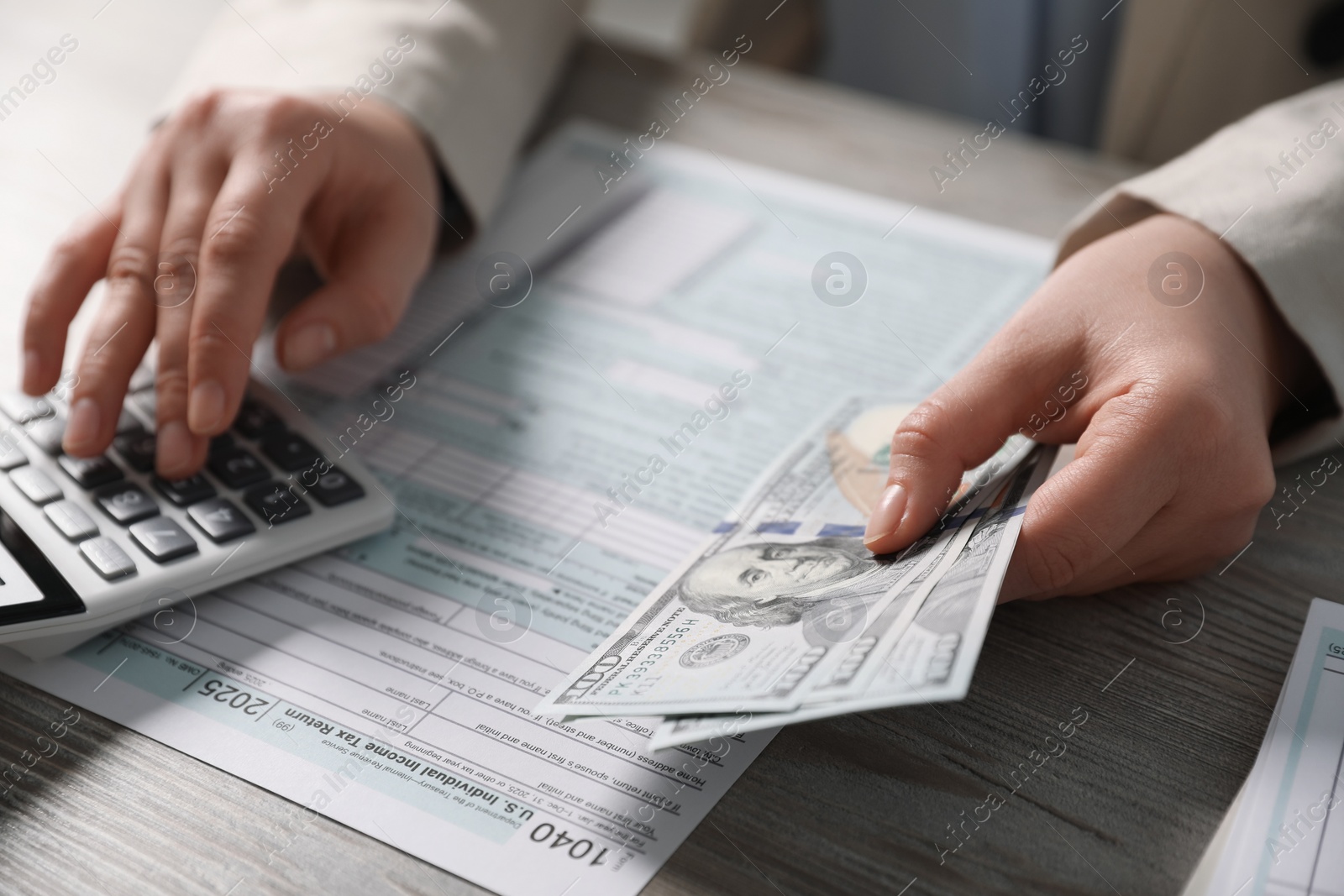 Photo of Payroll. Woman with dollar banknotes and calculator planning budget at wooden table, selective focus