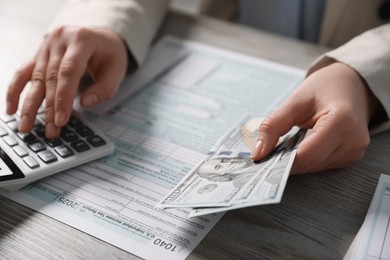 Payroll. Woman with dollar banknotes and calculator planning budget at wooden table, selective focus