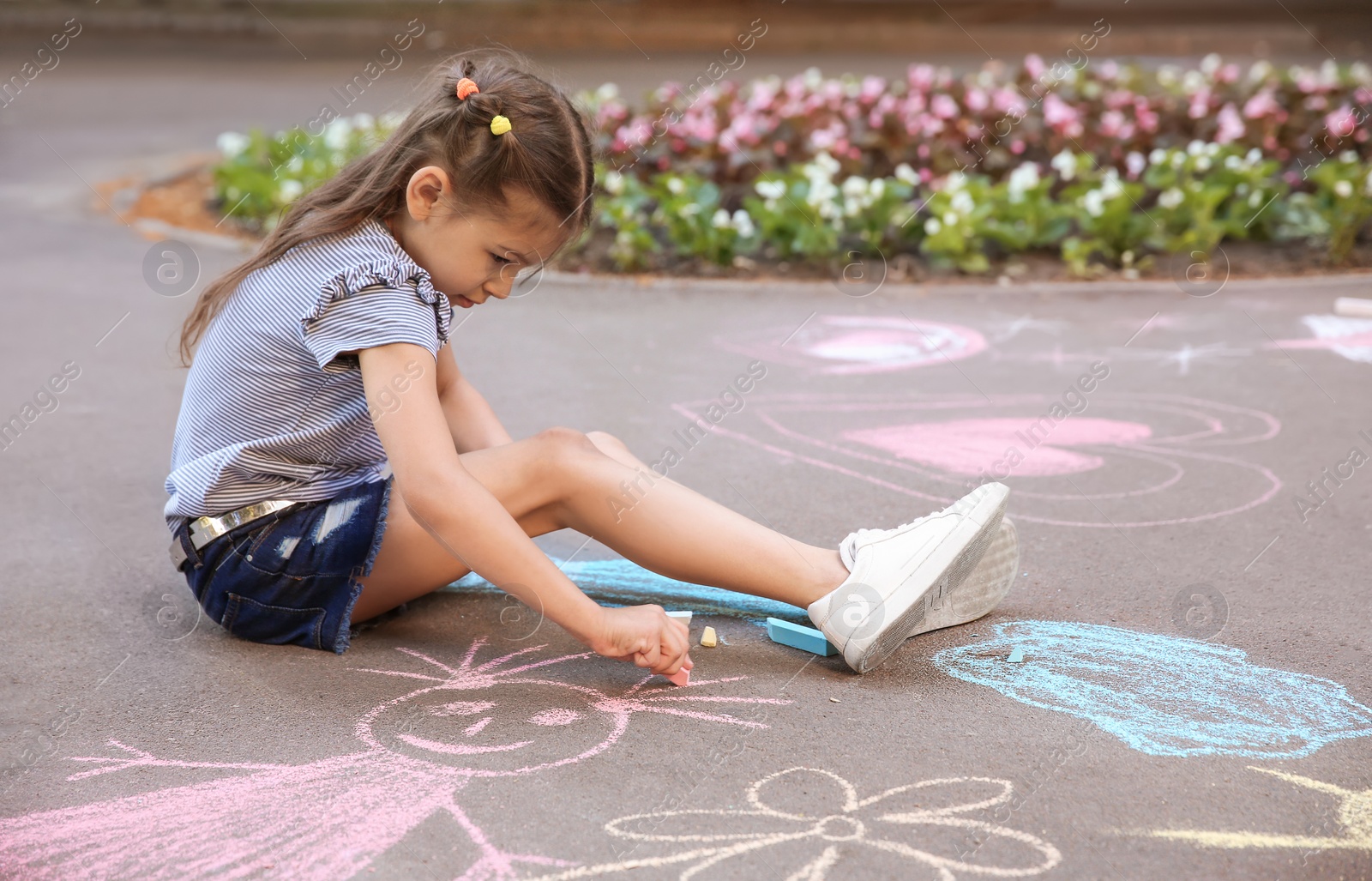 Photo of Little child drawing with colorful chalk on asphalt