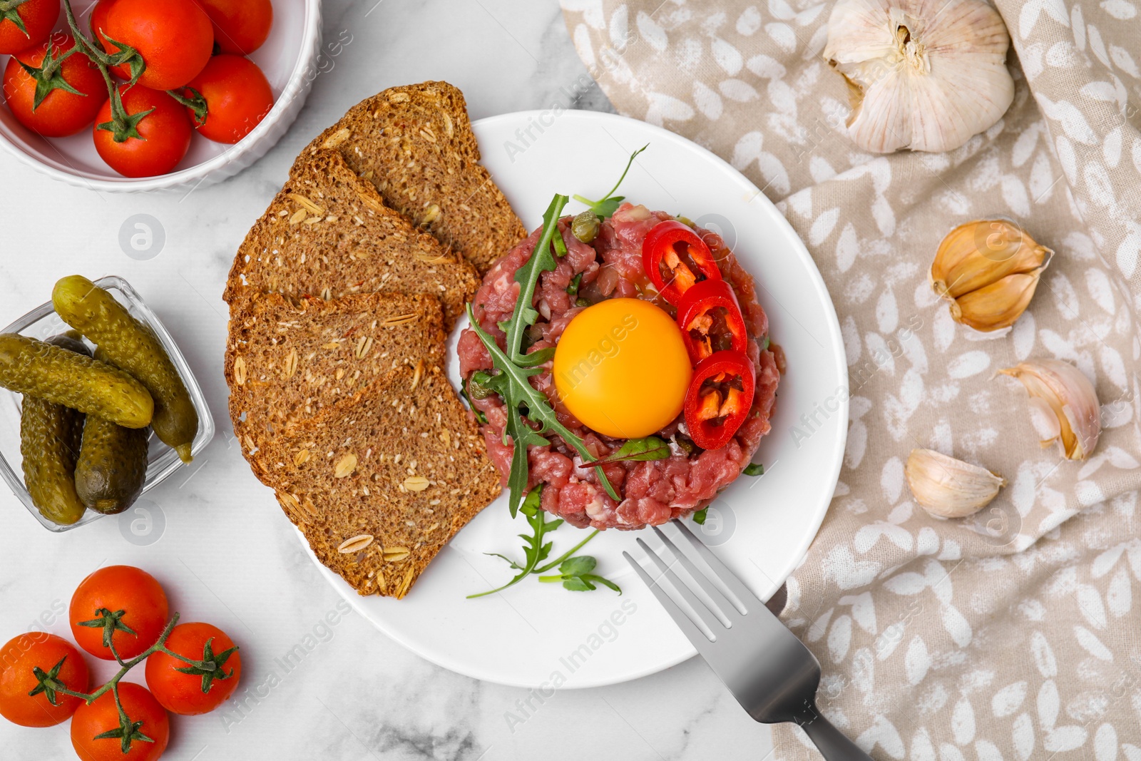 Photo of Tasty beef steak tartare served with yolk and other accompaniments on white marble table, flat lay