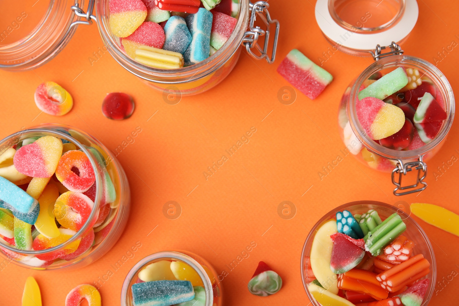 Photo of Frame of tasty jelly candies in jars on orange background, flat lay. Space for text