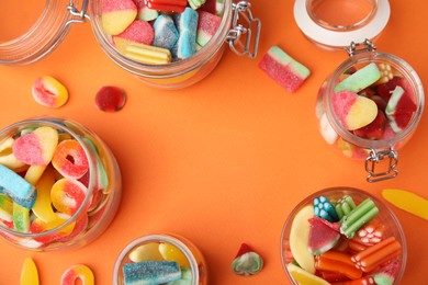 Photo of Frame of tasty jelly candies in jars on orange background, flat lay. Space for text