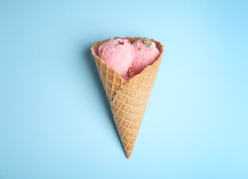 Photo of Delicious ice cream in wafer cone on blue background, top view