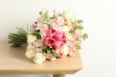 Photo of Beautiful bouquet of fresh flowers on wooden table near light wall. Space for text