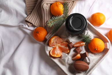 Photo of Delicious ripe tangerines, cup with drink and chocolates on white bedsheet, flat lay. Space for text