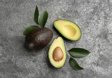 Whole and cut avocados with green leaves on grey table, flat lay