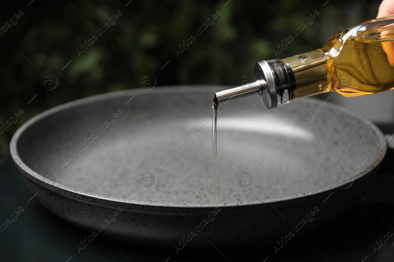 Photo of Woman pouring cooking oil from bottle into frying pan, closeup