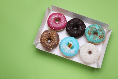 Photo of Box with different tasty glazed donuts on light green background, top view