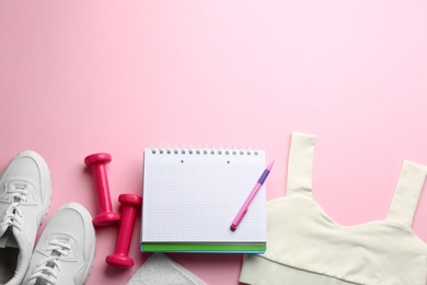 Photo of Flat lay composition with sportswear, notebook and dumbbells on pink background, space for text. Gym workout plan