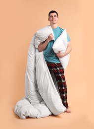 Photo of Happy man in pyjama holding pillow and blanket on beige background