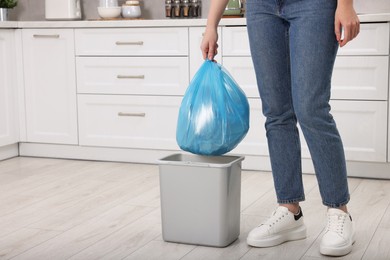 Photo of Woman taking garbage bag out of trash bin in kitchen, closeup. Space for text