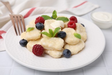 Plate of tasty lazy dumplings with berries, butter and mint leaves on white tiled table