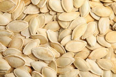 Photo of Raw unpeeled pumpkin seeds as background, top view