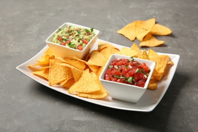 Photo of Plate with delicious mexican nachos chips and sauces on grey table