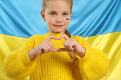 Photo of Little girl making heart with her hands near Ukrainian flag