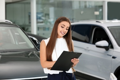 Photo of Saleswoman with clipboard standing in car salon