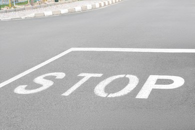 Photo of White sign Stop written on asphalt road in city
