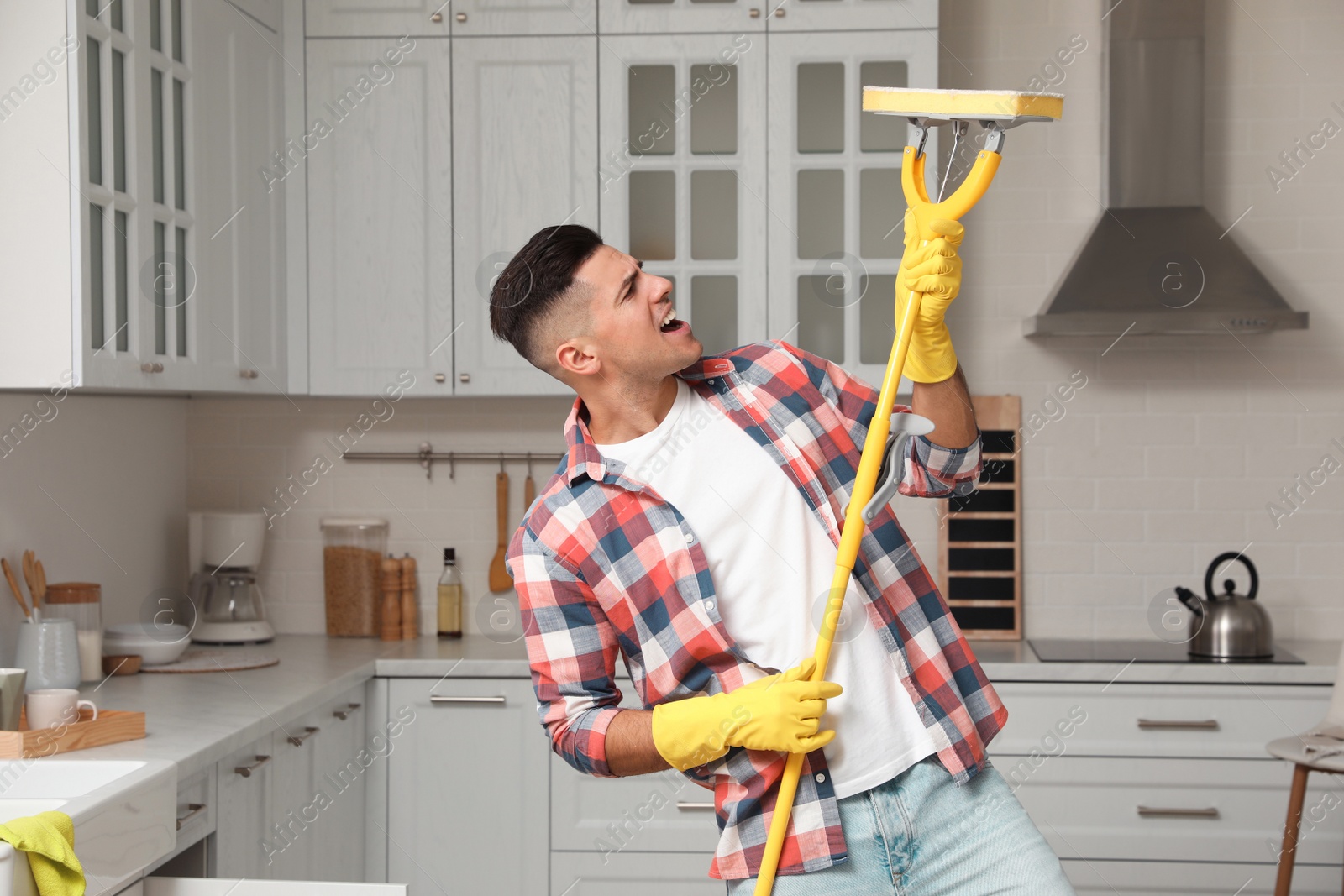 Photo of Man with mop singing while cleaning at home