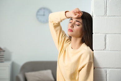 Stressed young woman near white brick wall at home. Space for text