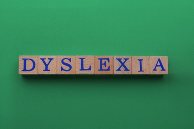 Wooden cubes with word Dyslexia on green background, flat lay