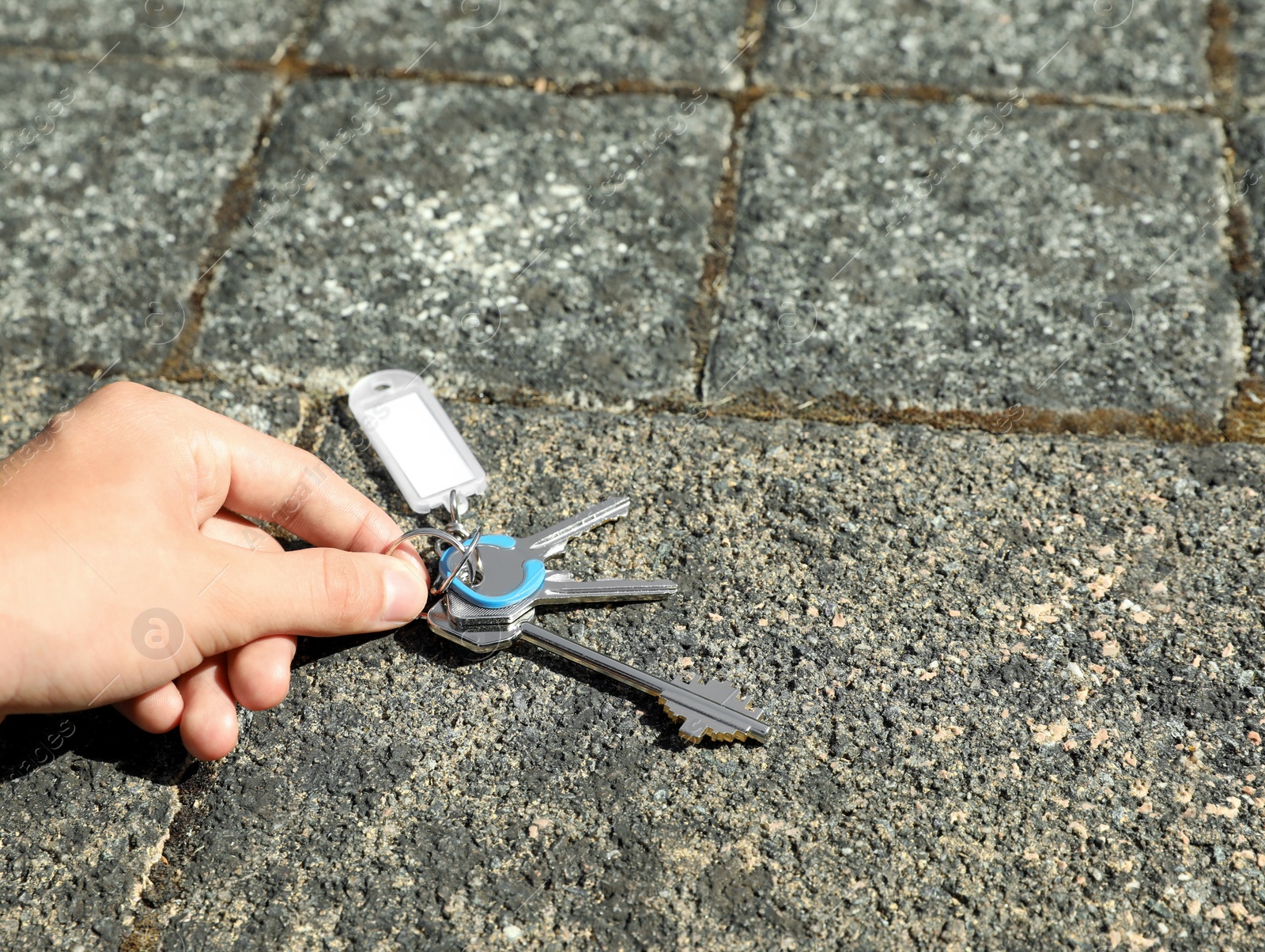 Photo of Woman picking bunch of keys from pavement outdoors, closeup. Space for text