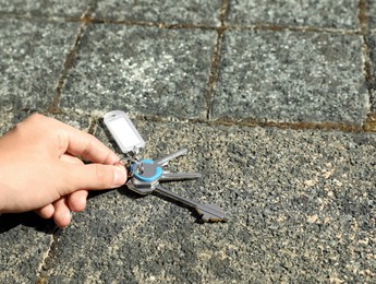 Woman picking bunch of keys from pavement outdoors, closeup. Space for text