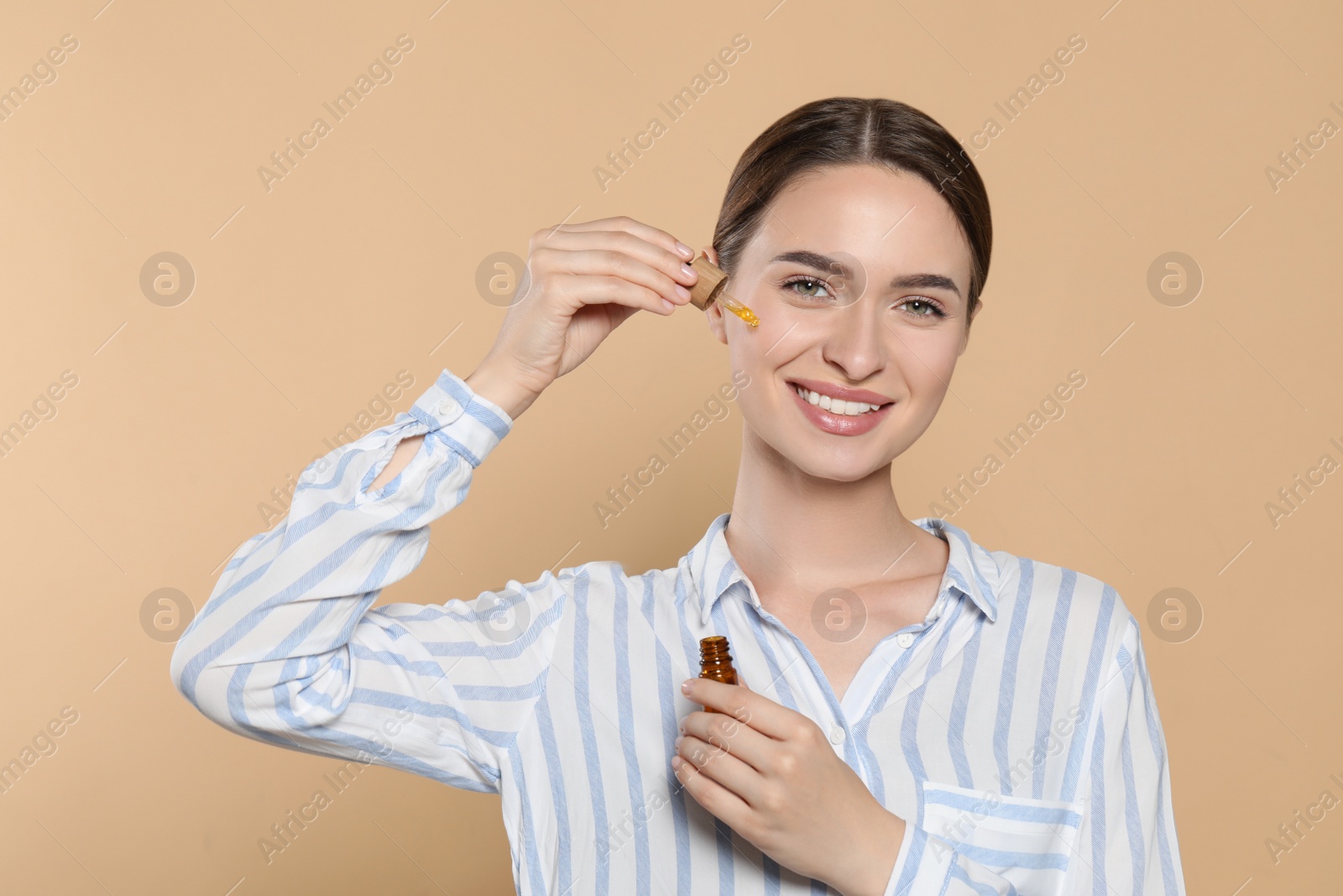 Photo of Young woman applying essential oil onto face on beige background