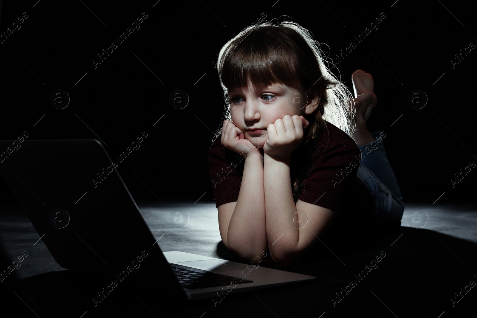 Photo of Little child in front of laptop on dark background. Cyber danger