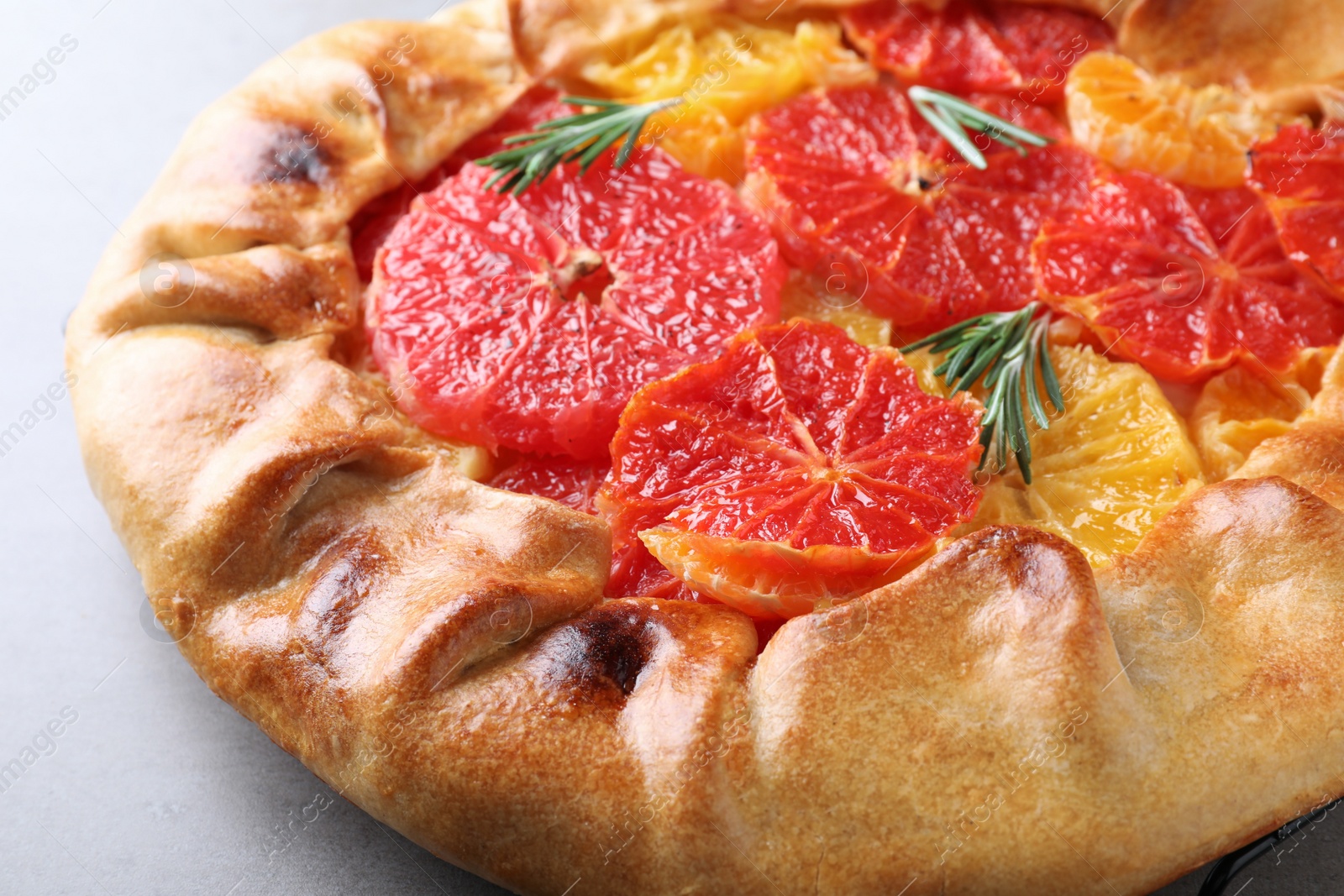 Photo of Tasty galette with citrus fruits and rosemary on table, closeup