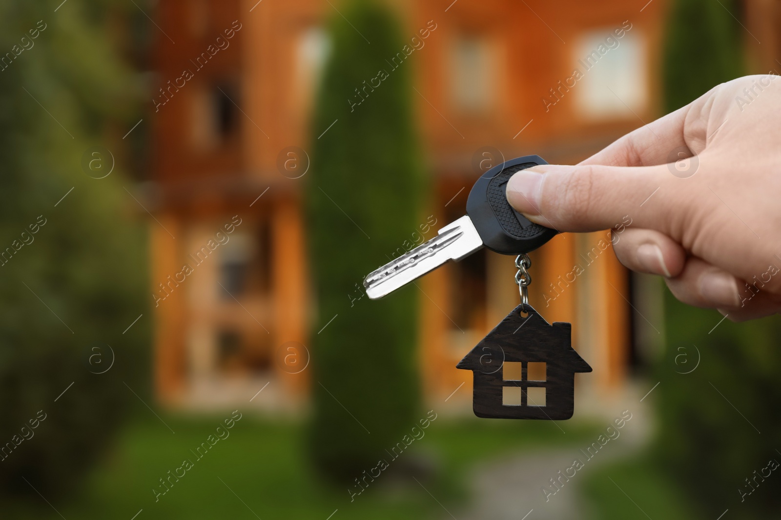 Photo of Real estate agent holding key and blurred house on background. Focus on hand