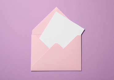 Letter envelope with card on violet background, top view