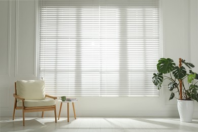 Photo of Cosy armchair and houseplant near large window with blinds in spacious room. Interior design