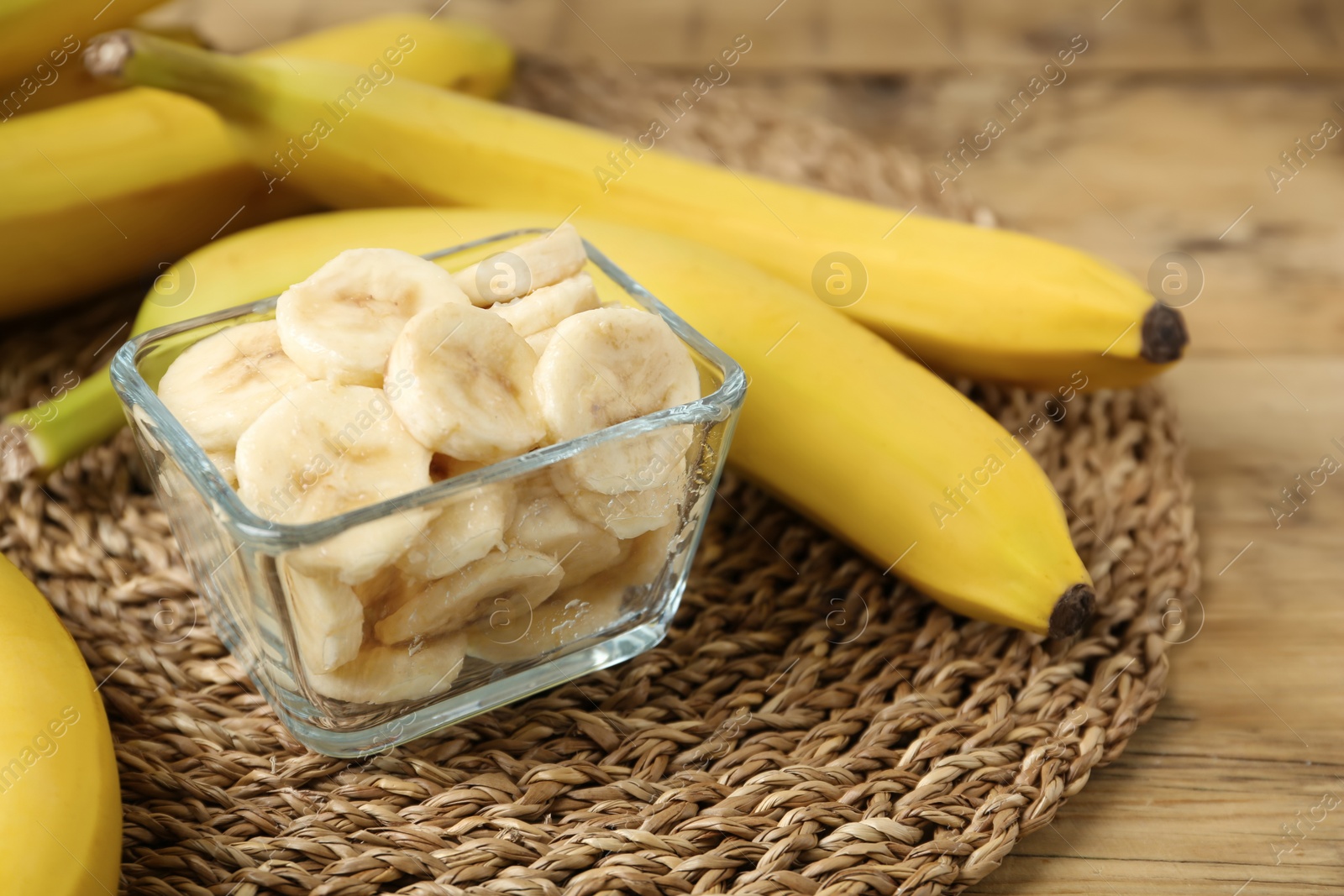 Photo of Bowl with cut bananas near whole fruits on wooden table, closeup