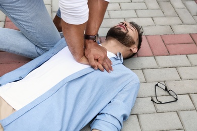 Passerby performing CPR on unconscious young man outdoors. First aid