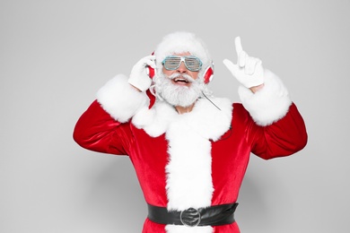 Santa Claus listening to Christmas music on color background