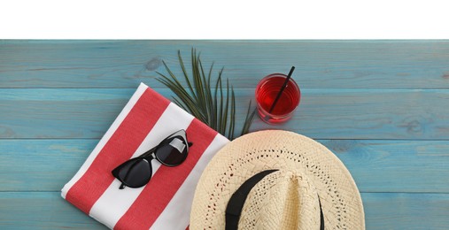 Light blue wooden surface with beach towel, straw hat, refreshing drink and sunglasses on white background, top view