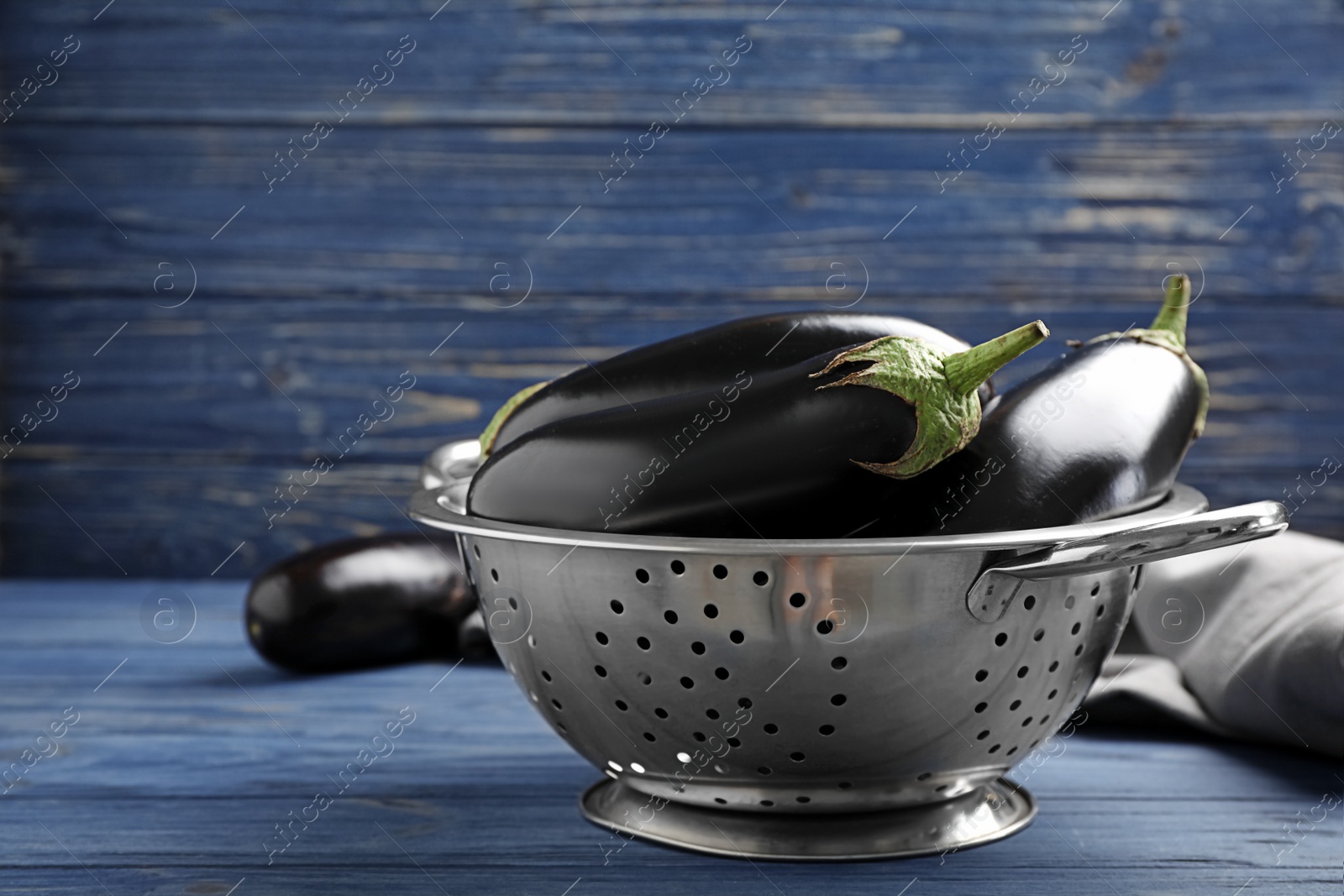 Photo of Colander with raw ripe eggplants on table