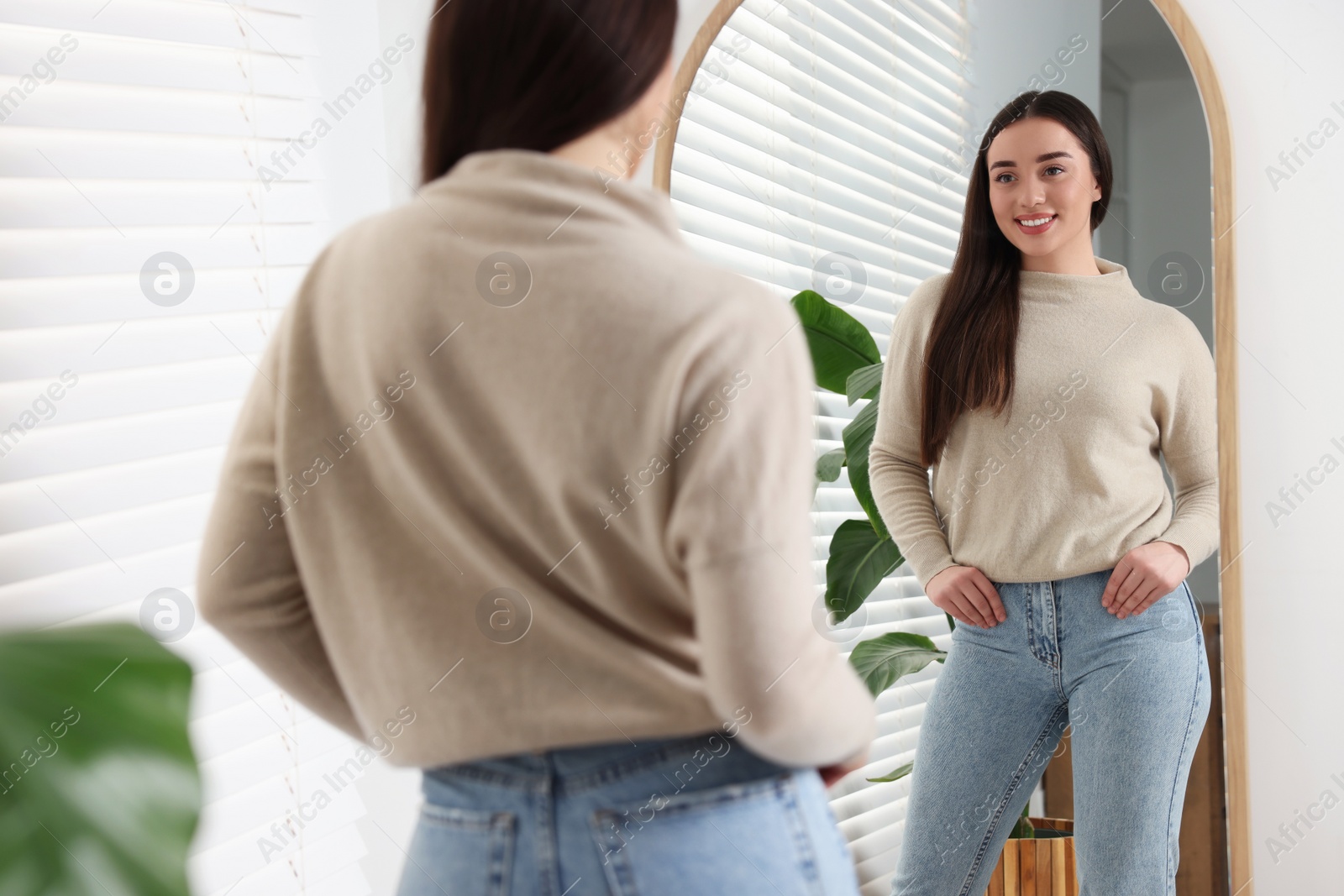 Photo of Young woman in stylish jeans near mirror indoors