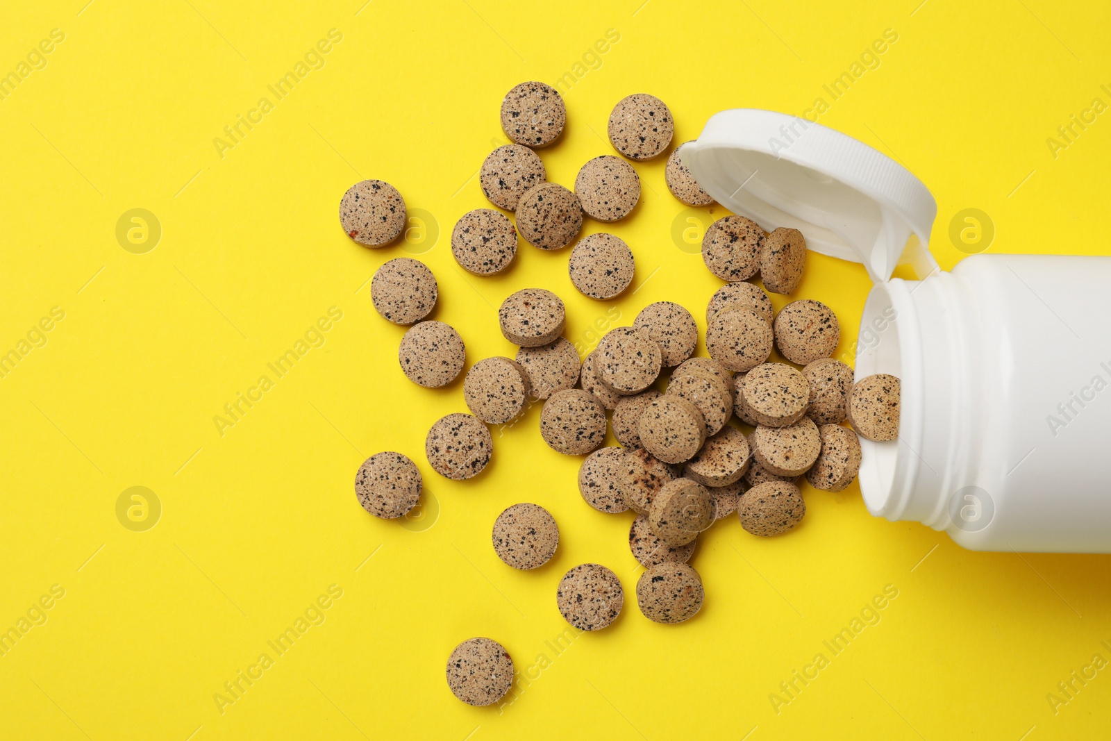 Photo of Vitamin pills and bottle on yellow background, top view