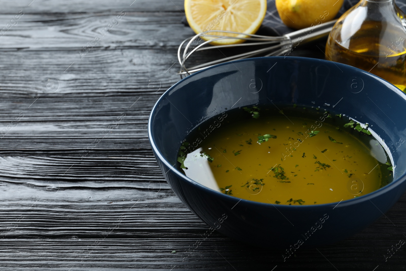 Photo of Bowl with lemon sauce on black wooden table, space for text. Delicious salad dressing