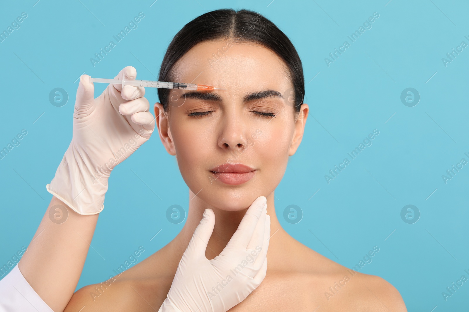 Photo of Doctor giving facial injection to young woman on light blue background. Cosmetic surgery