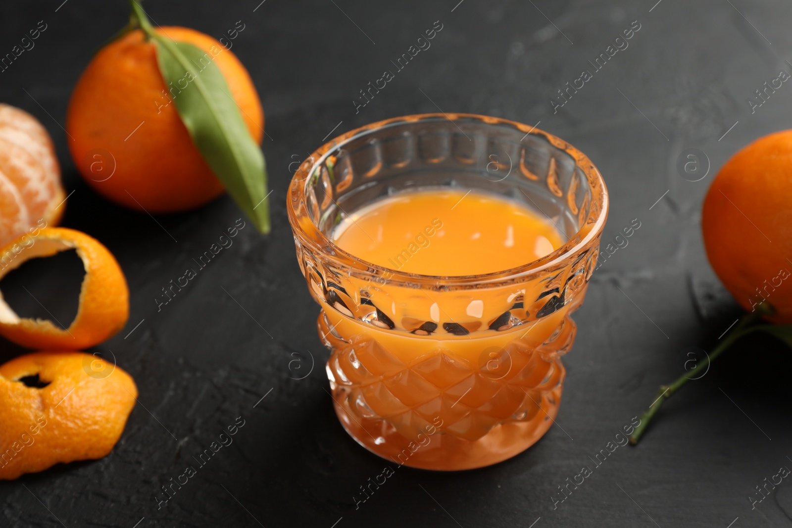 Photo of Tasty tangerine liqueur in glass and fresh fruits on black textured table, closeup