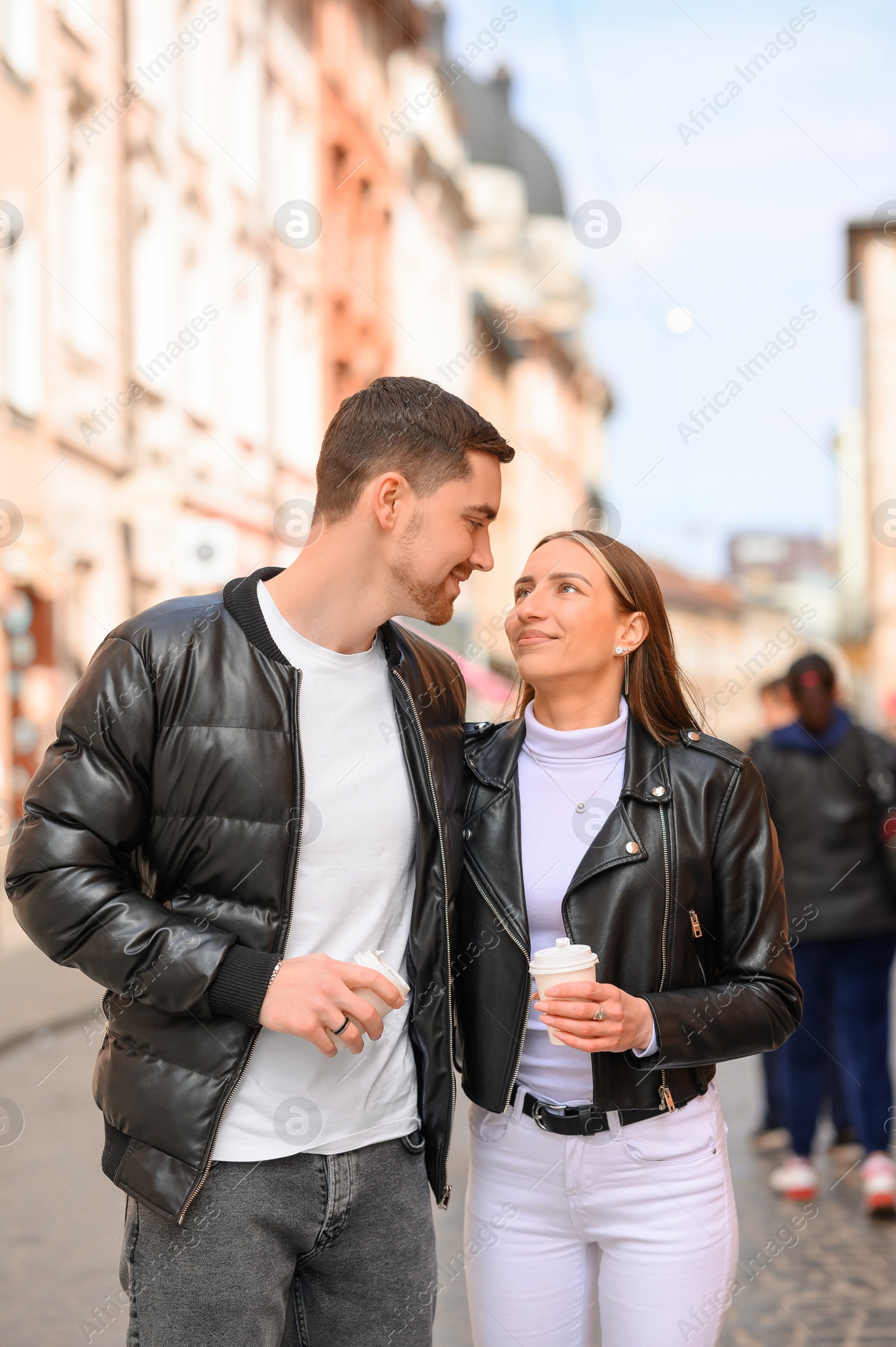 Photo of Lovely young couple with cups of coffee walking together on city street. Romantic date