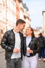 Photo of Lovely young couple with cups of coffee walking together on city street. Romantic date